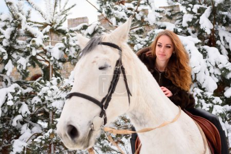 Téléchargez les photos : Winter coniferous forest with snow. A young girl with long hair in a fur coat riding a horse - en image libre de droit