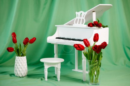 Foto de Un piano de cola blanco sobre un fondo verde. Tulipanes rojos en jarrones. Ubicación para fotos de primavera - Imagen libre de derechos