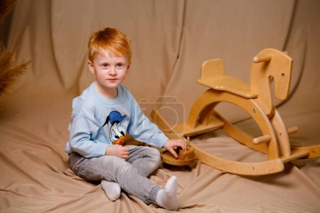Foto de Un chico pelirrojo en un suéter azul juega con juguetes de madera - Imagen libre de derechos