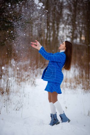 Foto de Una joven hermosa está tirando nieve en el parque en invierno. Clima nevado. Traje de mujer azul - Imagen libre de derechos