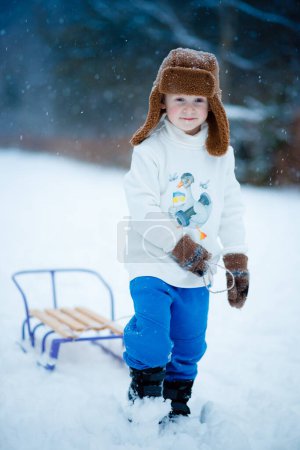Foto de Retrato de un niño de 4 años que conduce un trineo para bajar una colina y reírse en invierno - Imagen libre de derechos