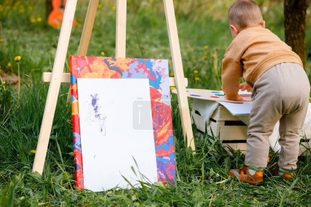 Foto de Un niño de 2 años dibuja un cuadro para su madre en un jardín floreciente. Pequeño artista - Imagen libre de derechos