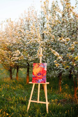 An easel with a picture in a garden with flowering trees