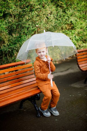 Children's walk. Brown suit. Green garden. Transparent umbrella