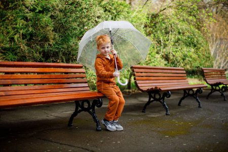 La marche des enfants. Costume marron. Jardin vert. Parapluie transparent