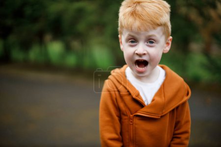 Foto de Un niño de 4 años de pelo rojo se ríe con los ojos cerrados. Retrato de un niño riendo. Niño muy emocional - Imagen libre de derechos