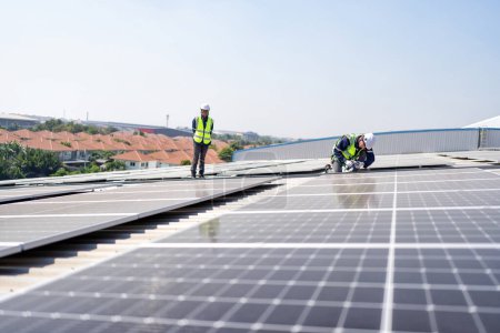 Foto de Ingeniero en azotea arrodillado junto a paneles solares fotovoltaicos con herramienta en mano para instalación - Imagen libre de derechos