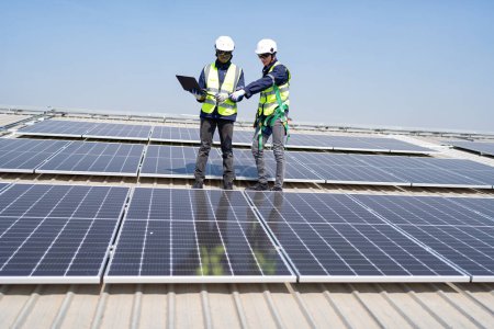 Téléchargez les photos : Ingénieur sur le toit stand à côté de panneaux solaires discussion avec l'équipe vérifier ordinateur portable pour l'installation - en image libre de droit