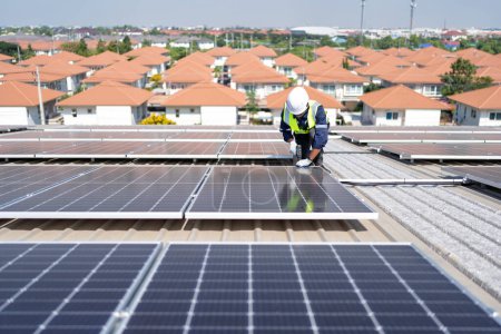 Foto de Ingeniero en azotea arrodillado junto a paneles solares fotovoltaicos con herramienta en mano para instalación - Imagen libre de derechos