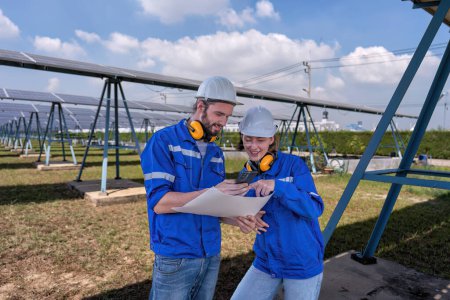 Téléchargez les photos : Ingénieurs à la ferme solaire à l'heure de pause regardant les médias sociaux drôles de téléphone mobile et rire - en image libre de droit
