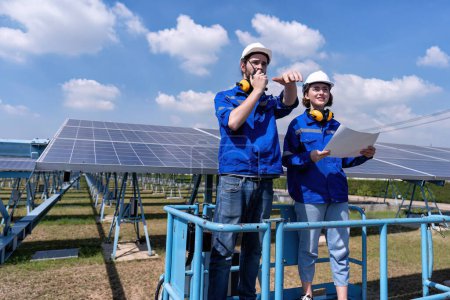Téléchargez les photos : Ingénieurs d'entretien à la ferme solaire stand sur ascenseur à ciseaux, inspection des panneaux solaires et des rapports radio - en image libre de droit