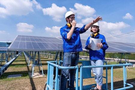Téléchargez les photos : Ingénieurs d'entretien à la ferme solaire stand sur ascenseur à ciseaux, inspection des panneaux solaires et des rapports radio - en image libre de droit