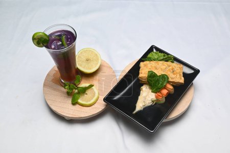 Téléchargez les photos : A glass of mocktail terong belanda on a wooden plate and a plate of nila puff pastry on a white cloth. - en image libre de droit
