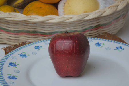 Téléchargez les photos : Red apples on a classic white plate with a basket of fruit in the background. - en image libre de droit