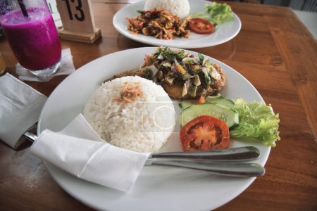 Photo for Nasi ayam pecak, a serving of pecak chicken rice on a wooden table. natural light. - Royalty Free Image