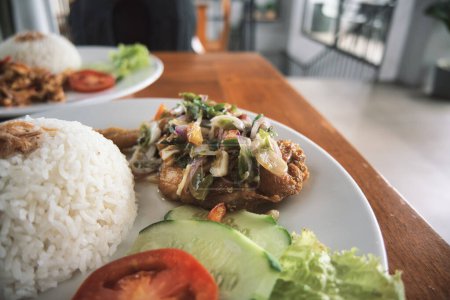 Téléchargez les photos : Nasi ayam pecak, a serving of pecak chicken rice on a wooden table. natural light. - en image libre de droit