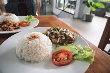 Photo for Nasi ayam pecak, a serving of pecak chicken rice on a wooden table. natural light. - Royalty Free Image