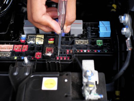 car mechanic checking the fuse connection using a multimeter and a test pen in the car fusebox