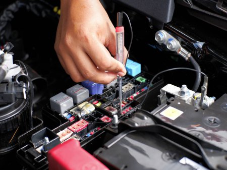 car mechanic checking the fuse connection using a multimeter and a test pen in the car fusebox