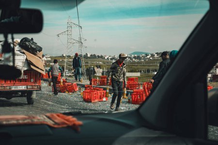 Photo for Tangier, Morocco - 15.03.2024: People looting the wreckage of a soda carrying truck. Coca-cola and Fanta bottles spilled on the ground. - Royalty Free Image