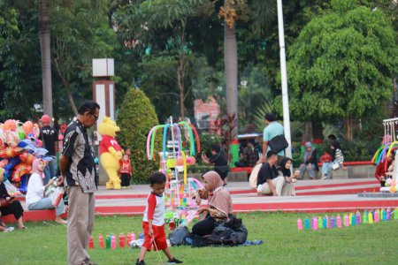 Foto de Kudus, diciembre de 2022. Fotografía de los visitantes sentados relajados disfrutando de la tarde en la hierba de la plaza de la ciudad de Kudus. - Imagen libre de derechos