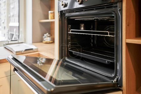  Opened door at electric oven with air ventilation. Side view of modern technology appliance against kitchen furniture. High quality photo