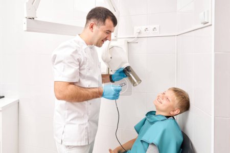Téléchargez les photos : Radiographe transmettant la radiographie dentaire à un garçon utilisant un appareil à rayons X numérique dans une clinique dentaire pédiatrique. Le dentiste prépare le garçon à une radiographie dentaire en clinique dentaire - en image libre de droit