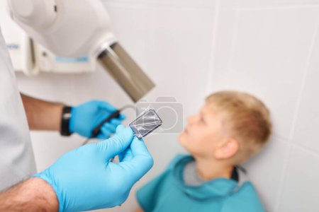 Photo for Radiographer taking teeth radiography to a boy using digital x-ray machine in pediatric dental clinic. Dentist prepares boy for tooth x-ray image in dental clinic - Royalty Free Image