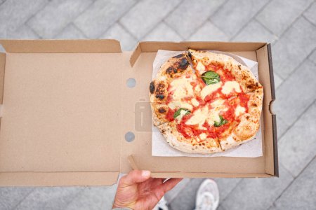 Photo for Pizza delivery concept. Baking in a cardboard box on a wooden background. Baked a delicious pizza Margarita in a traditional wood-burning oven in a Neapolitan restaurant, Italy. High quality photo - Royalty Free Image