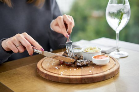 Photo for Lunch in a restaurant, a woman eats Pieces of liver cooked on the grill. Serving on a wooden Board. Barbecue restaurant menu, a series of photos of different meats. High quality photo - Royalty Free Image