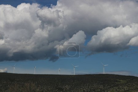 Photo for Against a backdrop of fluffy clouds and radiant sunshine, wind turbines stand tall, their blades slicing through the air to harness clean, renewable energy - Royalty Free Image