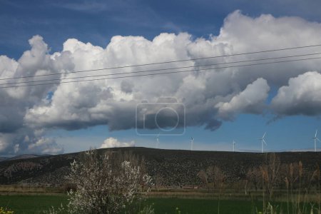 Vor dem Hintergrund flauschiger Wolken und strahlendem Sonnenschein ragen Windräder in die Höhe, deren Flügel sich durch die Luft schneiden, um saubere, erneuerbare Energien zu nutzen.
