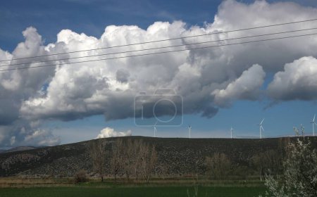 Vor dem Hintergrund flauschiger Wolken und strahlendem Sonnenschein ragen Windräder in die Höhe, deren Flügel sich durch die Luft schneiden, um saubere, erneuerbare Energien zu nutzen.