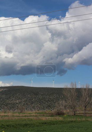 Photo for Against a backdrop of fluffy clouds and radiant sunshine, wind turbines stand tall, their blades slicing through the air to harness clean, renewable energy - Royalty Free Image