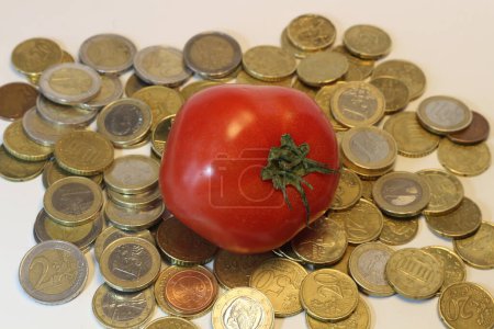 Téléchargez les photos : Une tomate perchée au sommet d'une pile de pièces symbolise l'intersection de l'inflation, de l'agriculture et du prix des produits - en image libre de droit