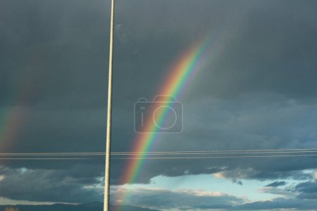 Embárcate en un viaje visual mientras captas la impresionante belleza de un arco iris con un telón de fondo de nubes dramáticas