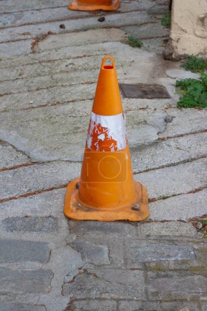This battered orange traffic cone stands as a weathered symbol of the wear and tear endured on the roads, serving as a reminder of safety measures and road maintenance