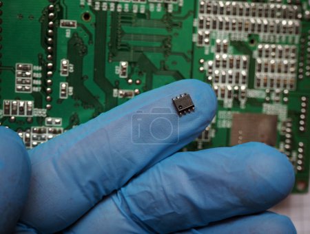 Photo for Gloved person hand holding a microchip on the circuit board. - Royalty Free Image