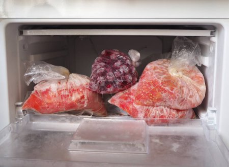 Foto de Frutas y verduras en bolsas en el congelador en casa. Cerezas congeladas y tomates en rodajas congelados - Imagen libre de derechos