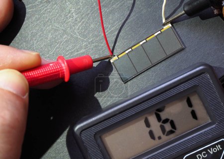 Foto de Tiny solar cell voltage test with multimeter under the sunlight. Photoelectric cells. Focused on cell. - Imagen libre de derechos