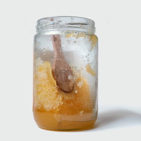 Glas mit kristallisiertem Honig isoliert auf einem grauen.