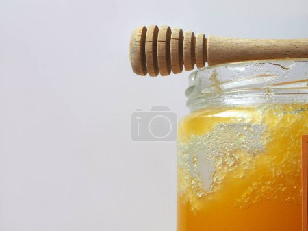 Photo for Crystallized honey in the glass jar on the gray background. Half of the honey jar, with wooden spoon and text area. - Royalty Free Image