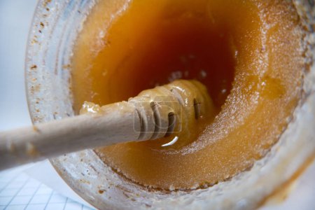 Caramelized honey dripping from a wooden spoon. Crystallized honey in a glass jar.