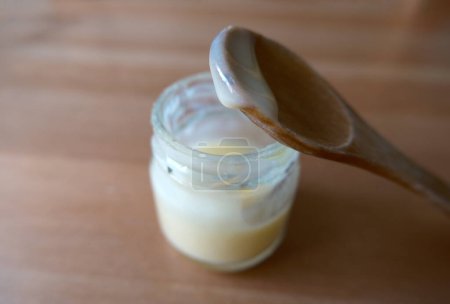 Harvested royal jelly in a little jar. It's also called bee milk. Focused on the drop in wooden spoon.