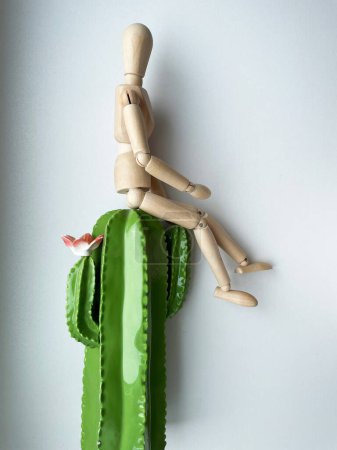 Téléchargez les photos : La marionnette en bois est assise sur un cactus. Photo de haute qualité - en image libre de droit