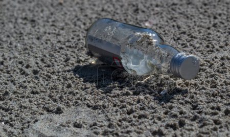 Foto de Una botella de vidrio en la arena. Botella de vidrio desechado acostado en la playa de arena. - Imagen libre de derechos