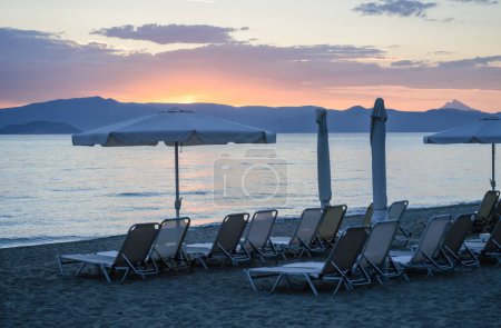 Blick auf den Strand mit Sonnenschirmen und Liegestühlen in der kleinen Stadt Pefkochori, am Morgen.