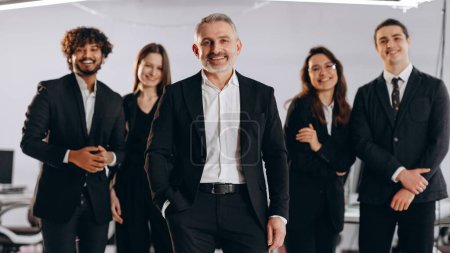 Photo for Smiling company executive with his team. Front view of laughing businesspeople in black suit posing together. Group of happy managers. High quality photo - Royalty Free Image