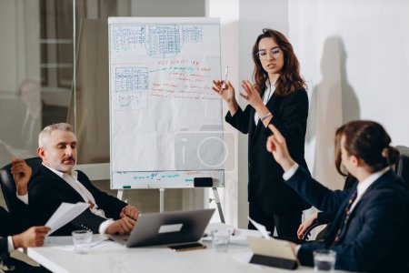 Foto de A team of businessmen at a business meeting in a conference room. The businesswoman offers her partners a new financial model of the company. High quality photo - Imagen libre de derechos