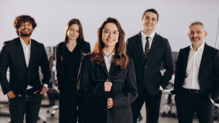 Photo for Confident businesswoman standing in front of her team. Woman team leader posing with smile with her coworkers in the background. Female leadership. High quality photo - Royalty Free Image